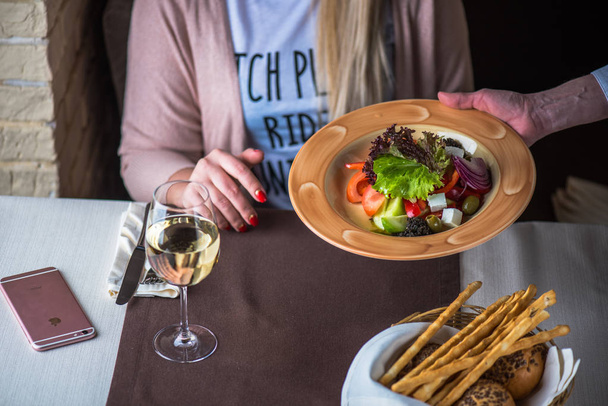 χέρι του γκαρσονιού που σερβίρει φρέσκια σαλάτα λαχανικών με φέτα σε γυναίκα στο εστιατόριο - Φωτογραφία, εικόνα