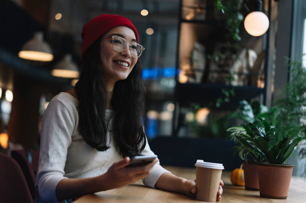 Iloinen aasialainen nainen käyttää matkapuhelinta, hymyilee, juo kahvia kahvilassa. Muotokuva onnellinen korealainen hipster tyttö kauniit kasvot tilalla matkapuhelin, lataaminen sovellus, online-ostoksia käteisellä takaisin, pankki
  - Valokuva, kuva