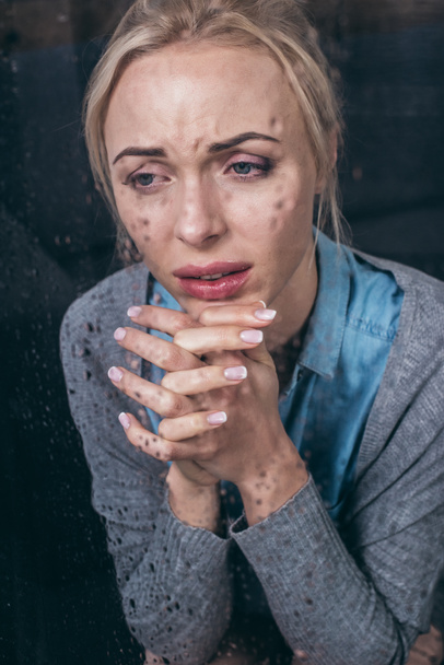 mujer adulta molesta con las manos dobladas llorando en casa a través de la ventana con gotas de lluvia
 - Foto, Imagen