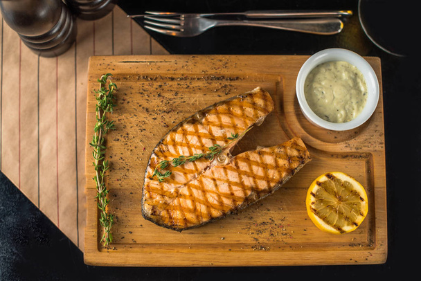 Grilled piece of salmon on wooden board with dip and lemon - Valokuva, kuva