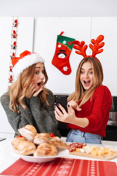 Two cheerful girls friends celebrating Christmas at home - Foto, afbeelding