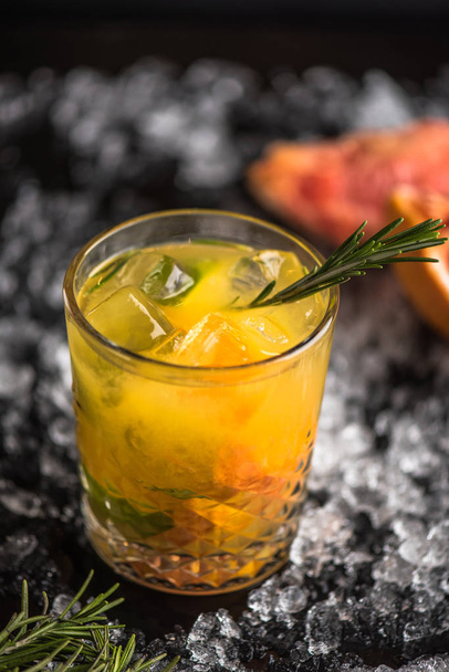 Cocktail in glass with grapefruit and rosemary on dark background with ice - Фото, зображення