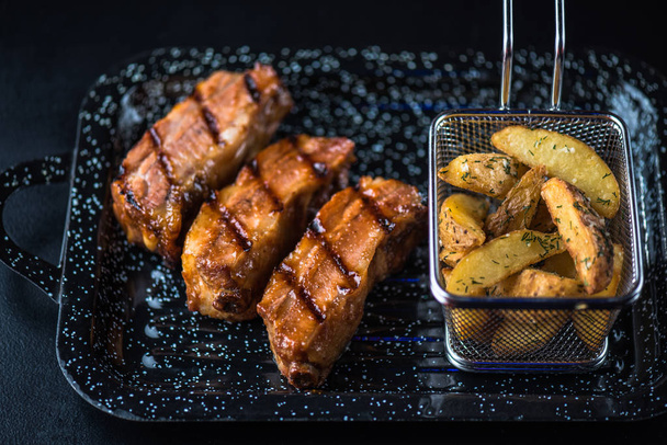 grilled meat steaks and roasted potato wedges served on black platter - 写真・画像
