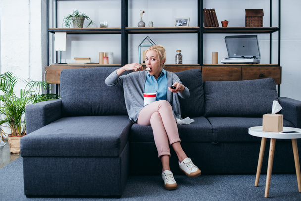 depressed woman eating ice cream while siitng on couch and watching tv at home alone - Fotografie, Obrázek