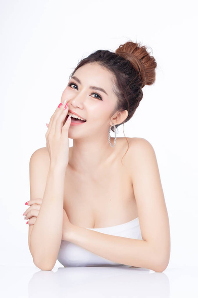 Porträt einer attraktiven Asiatin, die lächelnd auf weißem Hintergrund sitzt. gesunde Haut Frau natürliches Make-up Schönheit Gesicht Konzept. Verwendung als Produkt. - Foto, Bild