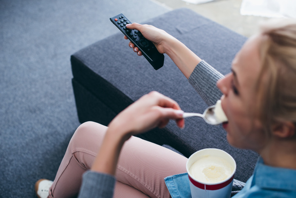 vista recortada de la mujer sentada en el sofá y comiendo helado mientras ve la televisión
 - Foto, Imagen