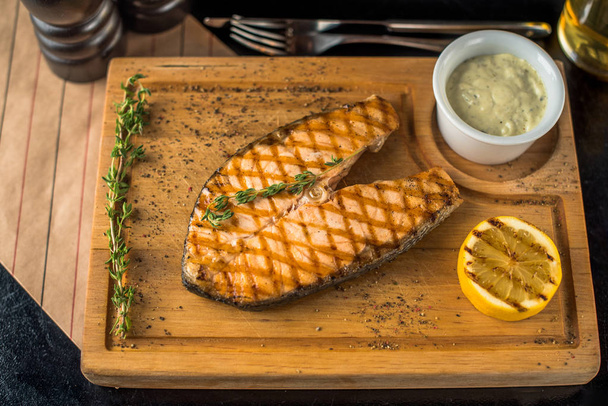 Grilled piece of salmon on wooden board with dip and lemon - Foto, imagen