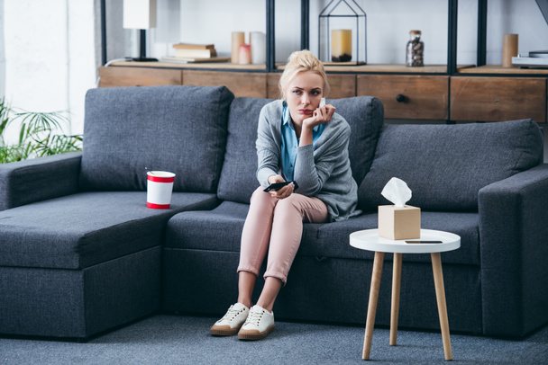 sad woman sittng on couch with bucket of ice cream and tissue box while watching tv in living room - Photo, Image