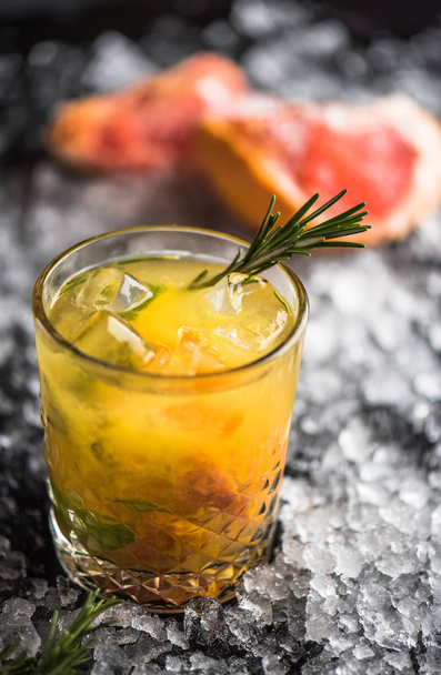 Cocktail in glass with grapefruit and rosemary on dark background with ice - 写真・画像
