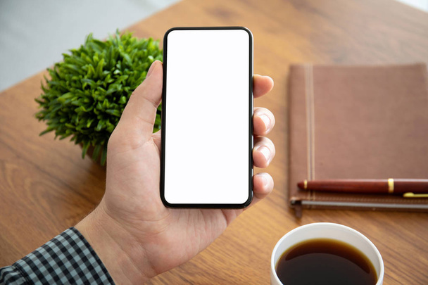 male hands holding phone with isolated screen above the table in office - Foto, Bild