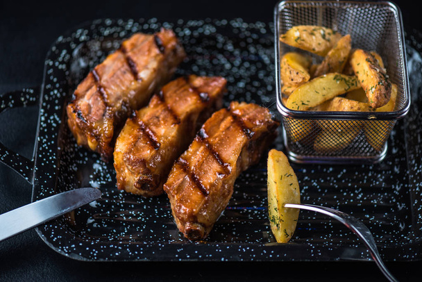 grilled meat steaks and roasted potato wedges served on black platter - Foto, Imagem
