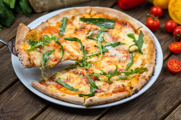 vista de cerca de la pizza gourmet con queso parmesano, rúcula y tomates en la mesa de madera
 - Foto, Imagen