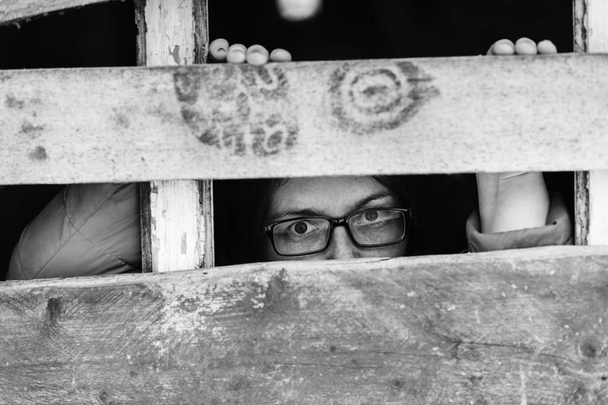 black and white photo of woman in eyeglasses standing behind wooden planks - Foto, Imagem