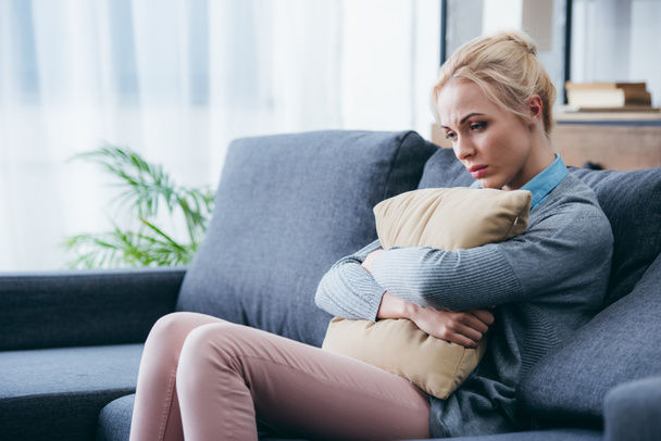 depressed woman sitting on couch and holding pillow at home - Photo, Image