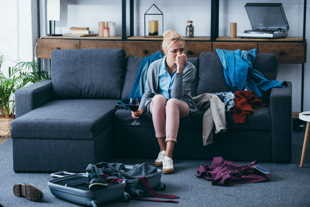 mujer deprimida sentada con un vaso de vino tinto y llorando mientras empaca en la sala de estar después de romper con su novio
 - Foto, Imagen