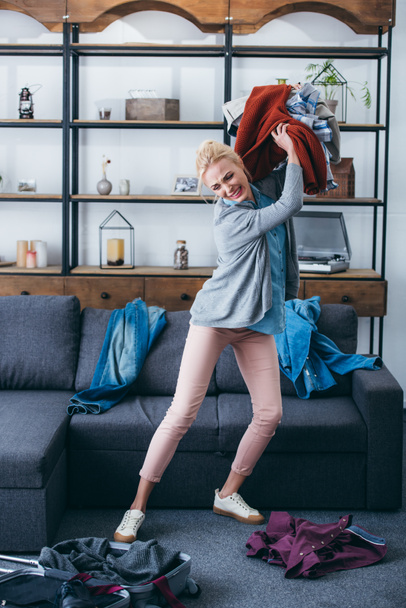 geïrriteerde vrouw werpen kleren in woonkamer na het breken met vriendje - Foto, afbeelding