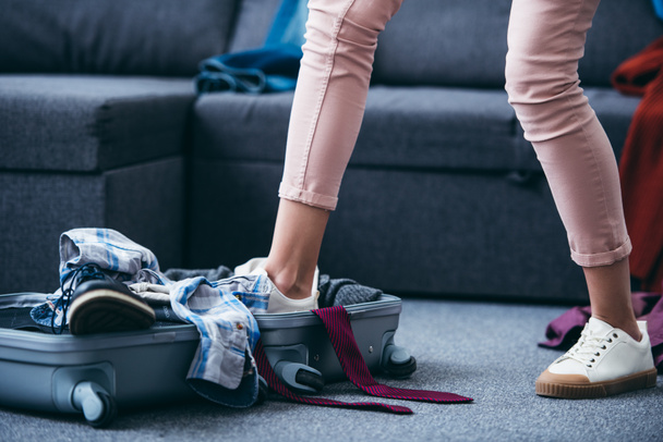 Ausgeschnittene Ansicht von Frau, die nach Trennung von Freund Kleidung in Koffer mit Bein schiebt - Foto, Bild