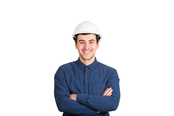 Веселый уверенный молодой человек инженер руки скрещенные носить защитный шлем улыбаясь глядя на камеру изолированы на белом фоне
. - Фото, изображение