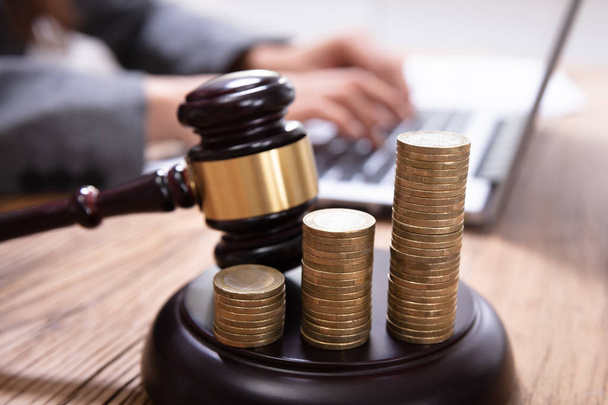 Close-up Of Increasing Coins And Mallet On Gavel With A Person Using Laptop At Background - Фото, зображення
