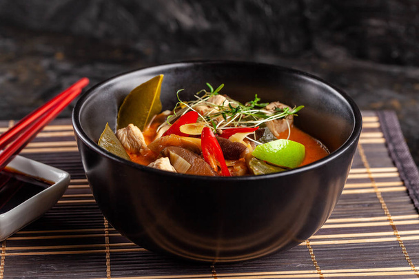 Concept of Asian cuisine. Thai soup Tom yam of chicken broth and coconut milk, mushrooms, chicken, chilli peppers, and vegetables. Japanese dish in black. Top view, copy space - Fotoğraf, Görsel