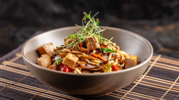 The concept of Japanese cuisine. Chinese noodles with chicken, grilled vegetables, and tofu in unagi sauce. Serving Asian dishes in the restaurant in a plate on a bamboo mat. Top view, copy space - Fotografie, Obrázek