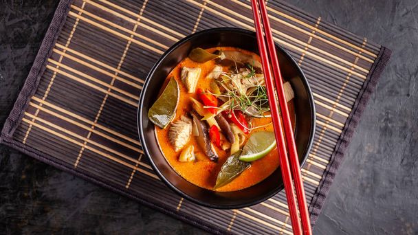 Concept of Asian cuisine. Thai soup Tom yam of chicken broth and coconut milk, mushrooms, chicken, chilli peppers, and vegetables. Japanese dish in black. Top view, copy space - Photo, Image