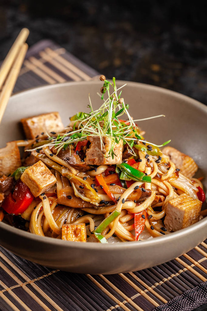 The concept of Japanese cuisine. Chinese noodles with chicken, grilled vegetables, and tofu in unagi sauce. Serving Asian dishes in the restaurant in a plate on a bamboo mat. Top view, copy space - Fotografie, Obrázek