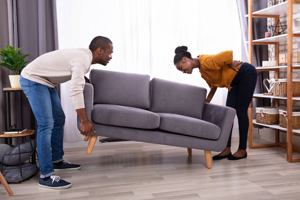 African Man Looking At His Wife Suffering From Back Pain While Lifting Sofa - Φωτογραφία, εικόνα
