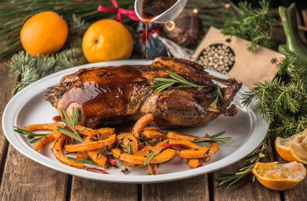 öntés szósz a karácsonyi sült kacsa mártással szolgálják fel, a tál a sütőtök és a narancs, a fából készült asztal - Fotó, kép