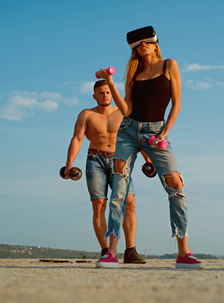 Woman wear VR headset. Woman athlete use simulator for training. Woman bodybuilder exercise with dumbbells with sportsman. Woman and man on blue sky. Experiencing virtual reality - Fotoğraf, Görsel