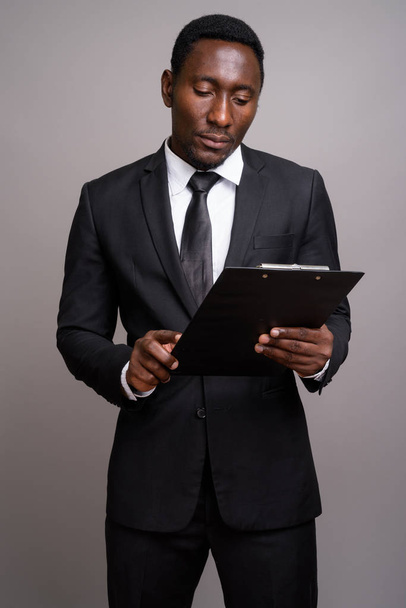 Young handsome African businessman against gray background - 写真・画像