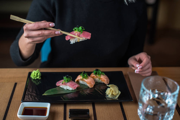 close-up of woman eating japanise nigiri sushi served on black plate at table - 写真・画像