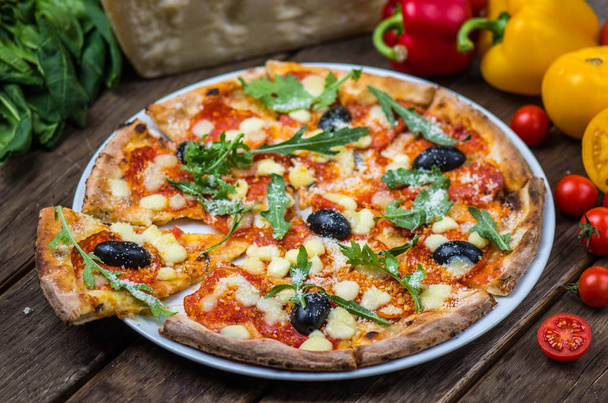 Italiaanse pizza met rucola en olijven geserveerd op plaat op houten tafel - Foto, afbeelding