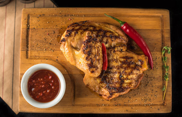 Pollo a la parrilla servido sobre tabla de madera con salsa picante y chiles
 - Foto, Imagen