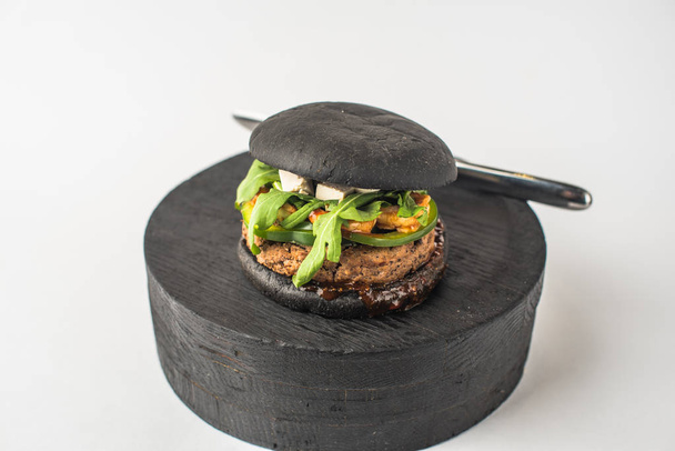 Black beef burger served on piece of wood on white background - Фото, изображение
