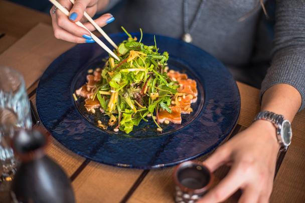 крупным планом женщина ест рыбные сашими и салат с палочками для еды
 - Фото, изображение