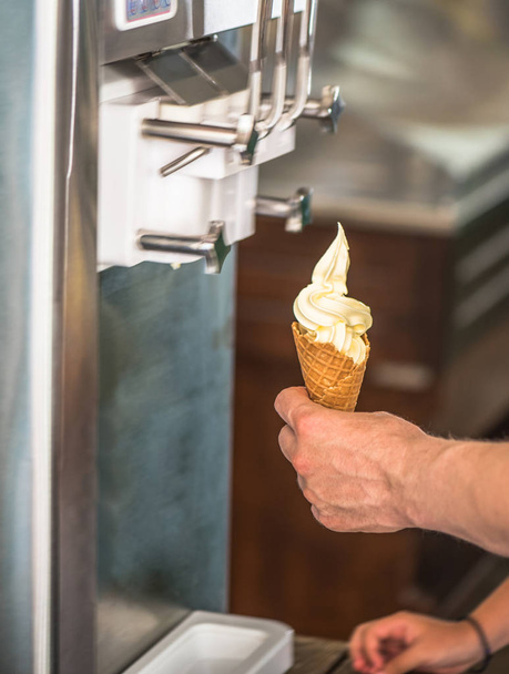 human hands putting ice cream in waffle cone with machine - Fotó, kép