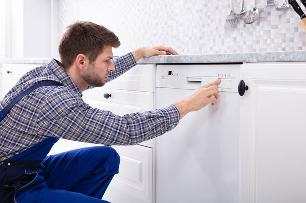 Young Serviceman Pressing Button Of Dishwasher In Kitchen - Foto, Imagen