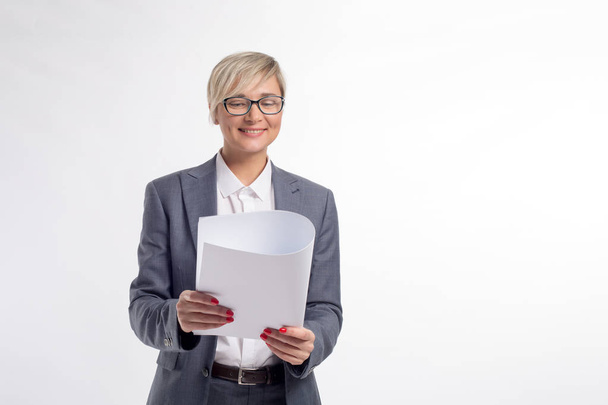 Femme d'affaires d'âge moyen, 40 ans, en chemise blanche, costume gris et lunettes, avec une manucure rouge, tient un papier Whatman blanc sur fond blanc
 - Photo, image