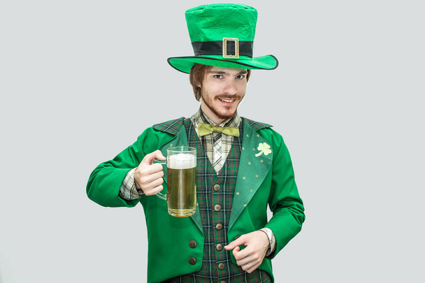 Happy young man in green saint Patricks suit holding mug of beer. He look on camera and smile. Guy confident and positive. Isolated on green background. - Photo, Image