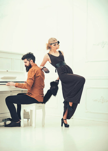 Bearded man with stylish hair playing piano while pretty girl in twenties dress and fur collar leaning on him isolated on white background - 写真・画像