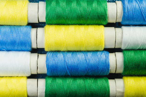 Bobinas de hilo de coser azul, amarillo, verde y blanco dispuestas en hileras sobre denim
 - Foto, Imagen