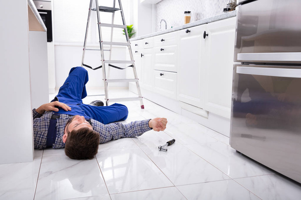 Close-up Of Unconscious Handyman Lying On Floor In Kitchen - Фото, изображение