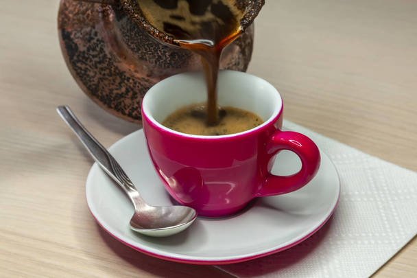 Black coffee flows from a cezve in a bright pink coffee cup - Foto, Imagem