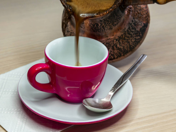 Black coffee flows from a cezve in a bright pink coffee cup - Foto, immagini