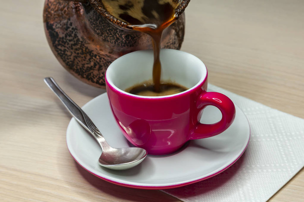 Black coffee flows from a cezve in a bright pink coffee cup - Foto, afbeelding