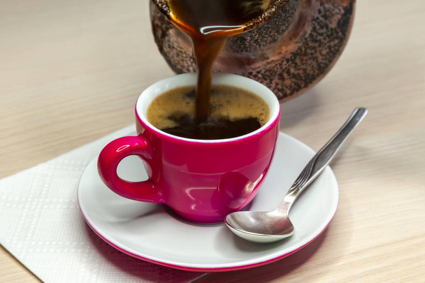 Black coffee flows from a cezve in a bright pink coffee cup - Foto, Bild