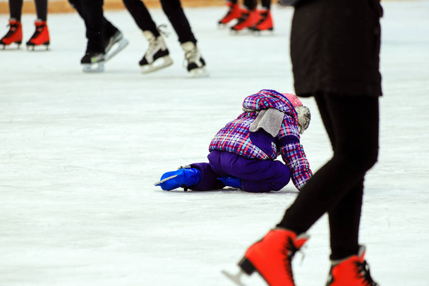 Un niño patina y cae en el hielo en la pista de patinaje Niños activos y deporte familiar, vacaciones de invierno. Clubes deportivos de la escuela, temporada fría
 - Foto, Imagen
