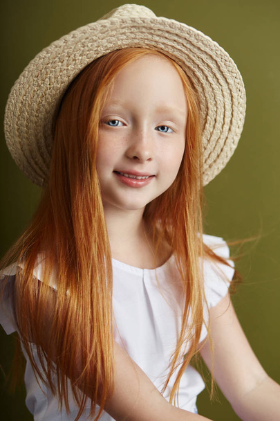 Uzun saç ve güzel büyük mavi gözlü güzel kızıl saçlı kız. Kızıl saçlı kız çocuk yaz giysileri zeytin renkli arka plan üzerinde poz. Parlak kırmızı saçlı Norveçli kız - Fotoğraf, Görsel