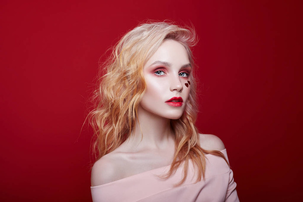 Slender blonde girl, perfect figure and long hair. Clean perfect face skin. Portrait of sexy fashion beautiful blonde woman with bright makeup posing on red crimson background - 写真・画像